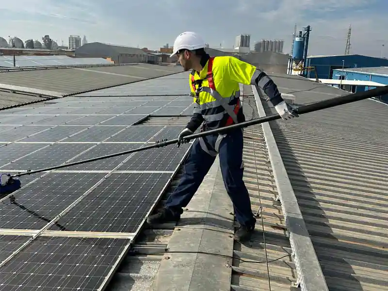 Operario con arnés y casco limpiando placas solares en una cubierta industrial