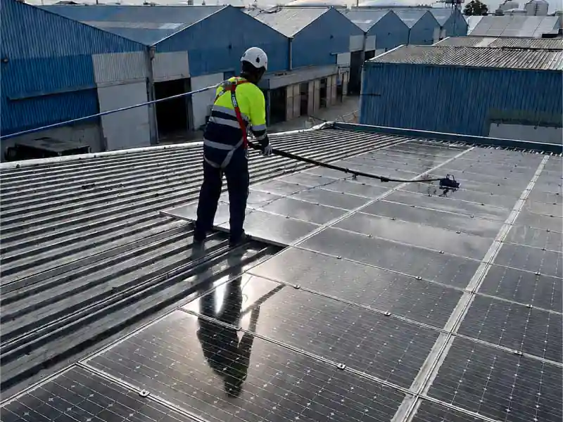 Operario limpiando placas solares con pértiga de agua osmotizada en una nave industrial