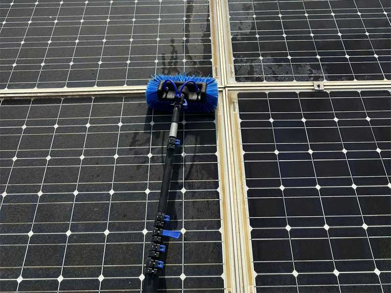 Operario limpiando placas solares con pértiga de agua